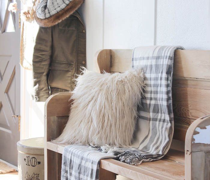 This simple farmhouse entryway is perfectly decorated for winter with large coat hooks, a rustic bench, and a place for snow-covered boots. See more photos at LoveGrowsWild.com